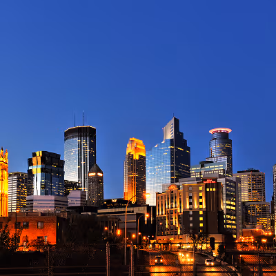 City skyline at dusk with illuminated buildings against a clear blue sky.